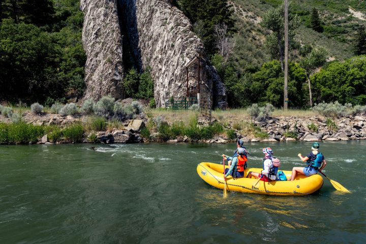 People rafting on a river in a yellow inflatable boat near rocky cliffs and greenery.