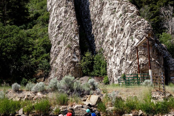A group in an orange raft paddles on a river near large rock formations.