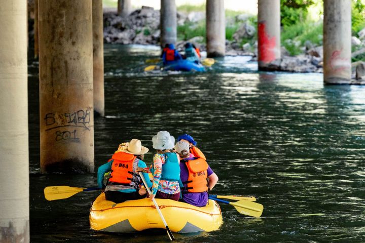 People in life jackets rafting under a bridge with concrete pillars.