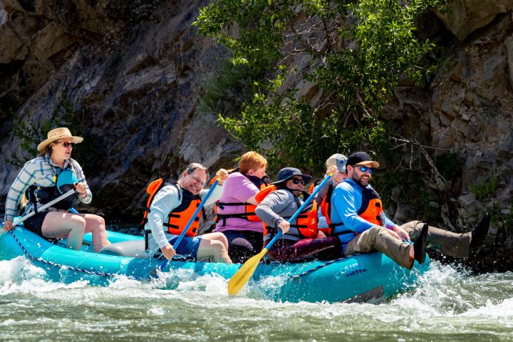 Group of people white-water rafting in a blue inflatable boat on a river.