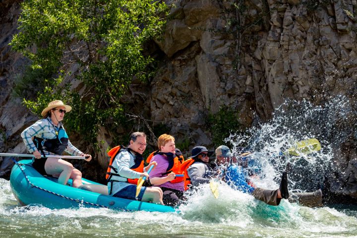 Group of people in life jackets rafting down a rocky river, with splashes of water around them.