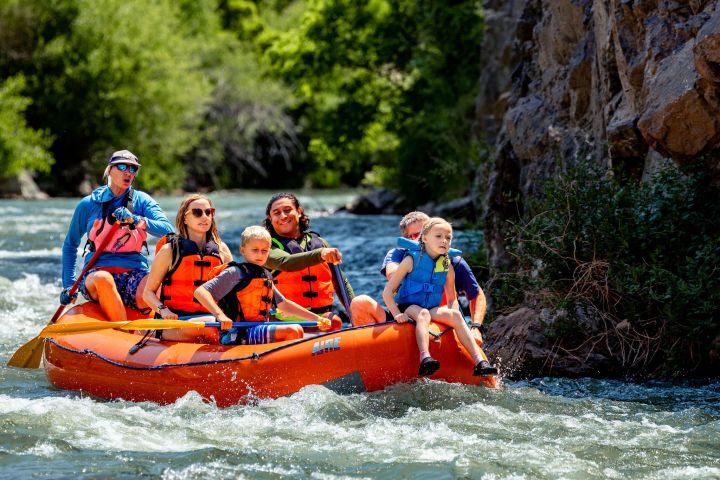 Group rafting on a river with life jackets, surrounded by trees and rocks.