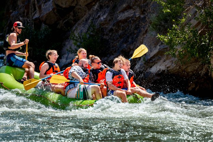 Group of people white-water rafting in a river, wearing life vests and paddling energetically.