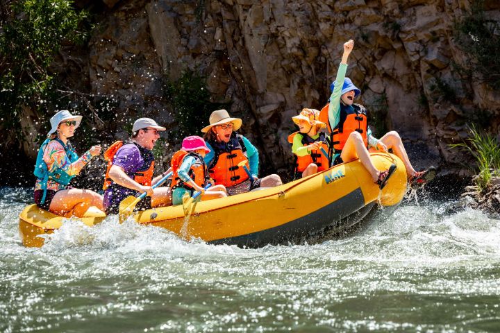Group of people in life jackets rafting on a river, with one person raising a fist in excitement.