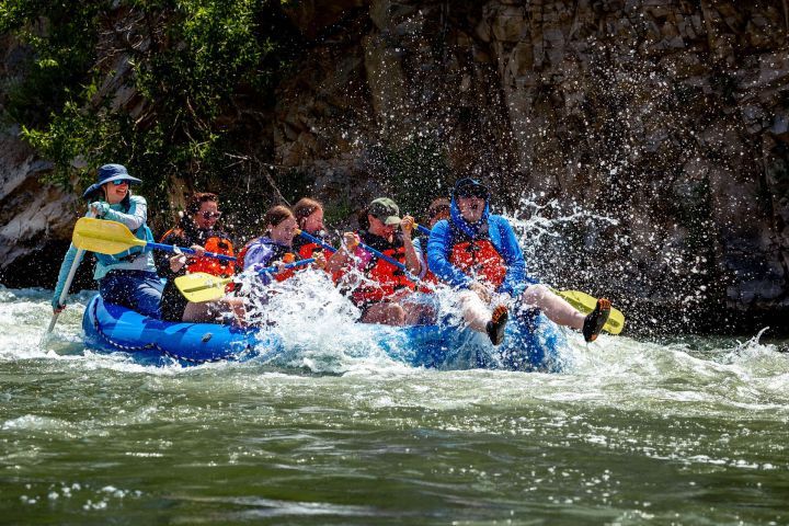 Group of people white water rafting on a river, splashing through rapids.