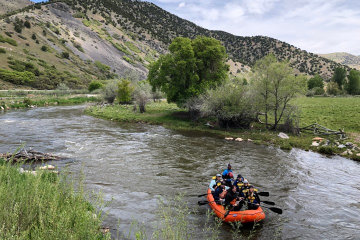 Group rafting on a river surrounded by trees and hills under a cloudy sky.