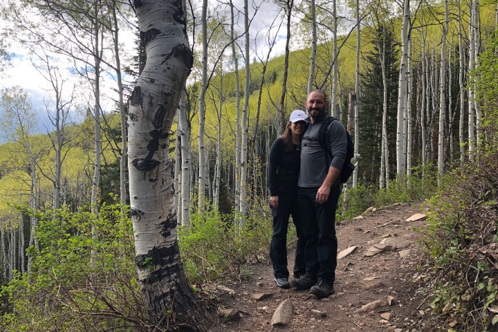 Two hikers on a forest trail with tall trees and green foliage.