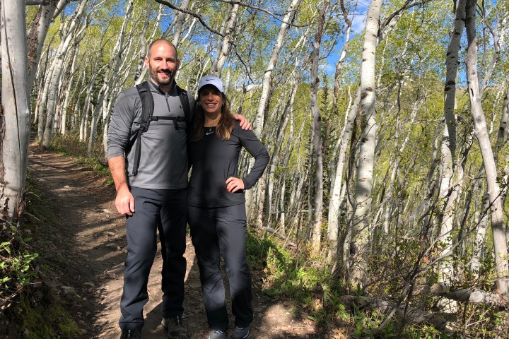 Two people in hiking gear on a forest trail surrounded by tall trees.
