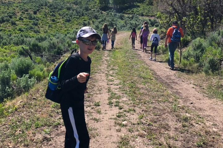 Children and adults hiking on a sunny trail with green hills.