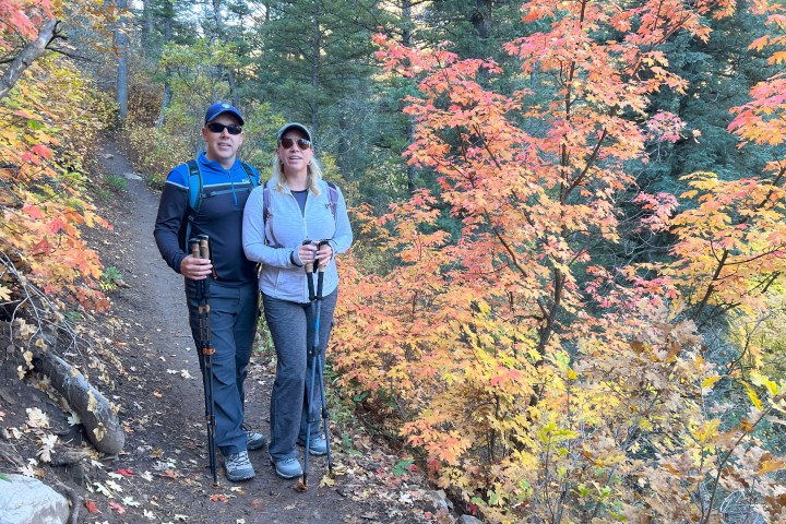 Two people hiking on a forest trail with colorful autumn leaves.