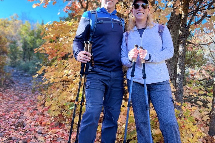 Couple hiking with poles in autumn forest with colorful leaves.